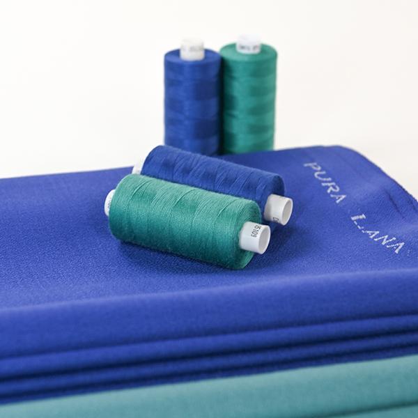 Présentation d'un tissu en crêpe pure laine et de bobines de fil assorties.